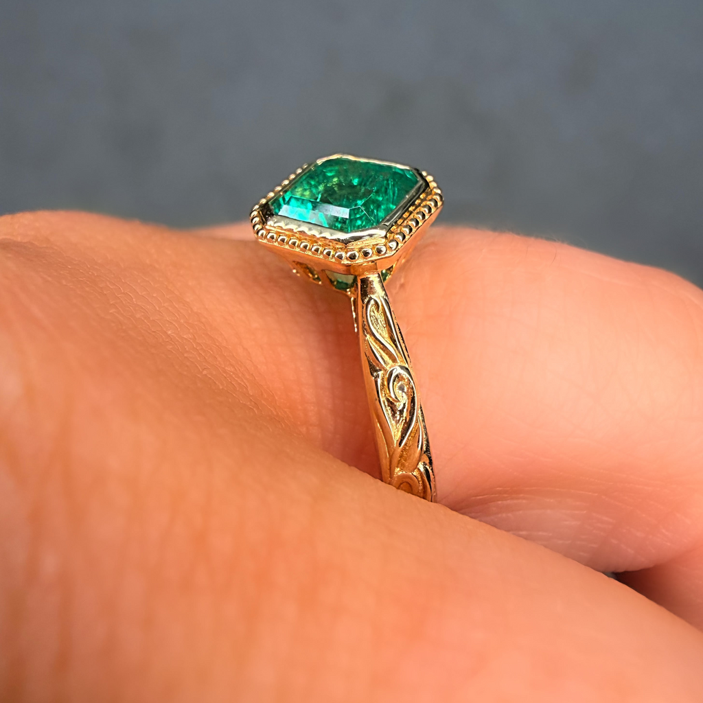 Gold ring with a green gemstone on a finger against a gray background
