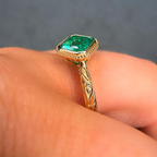 Gold ring with a green gemstone on a finger against a gray background