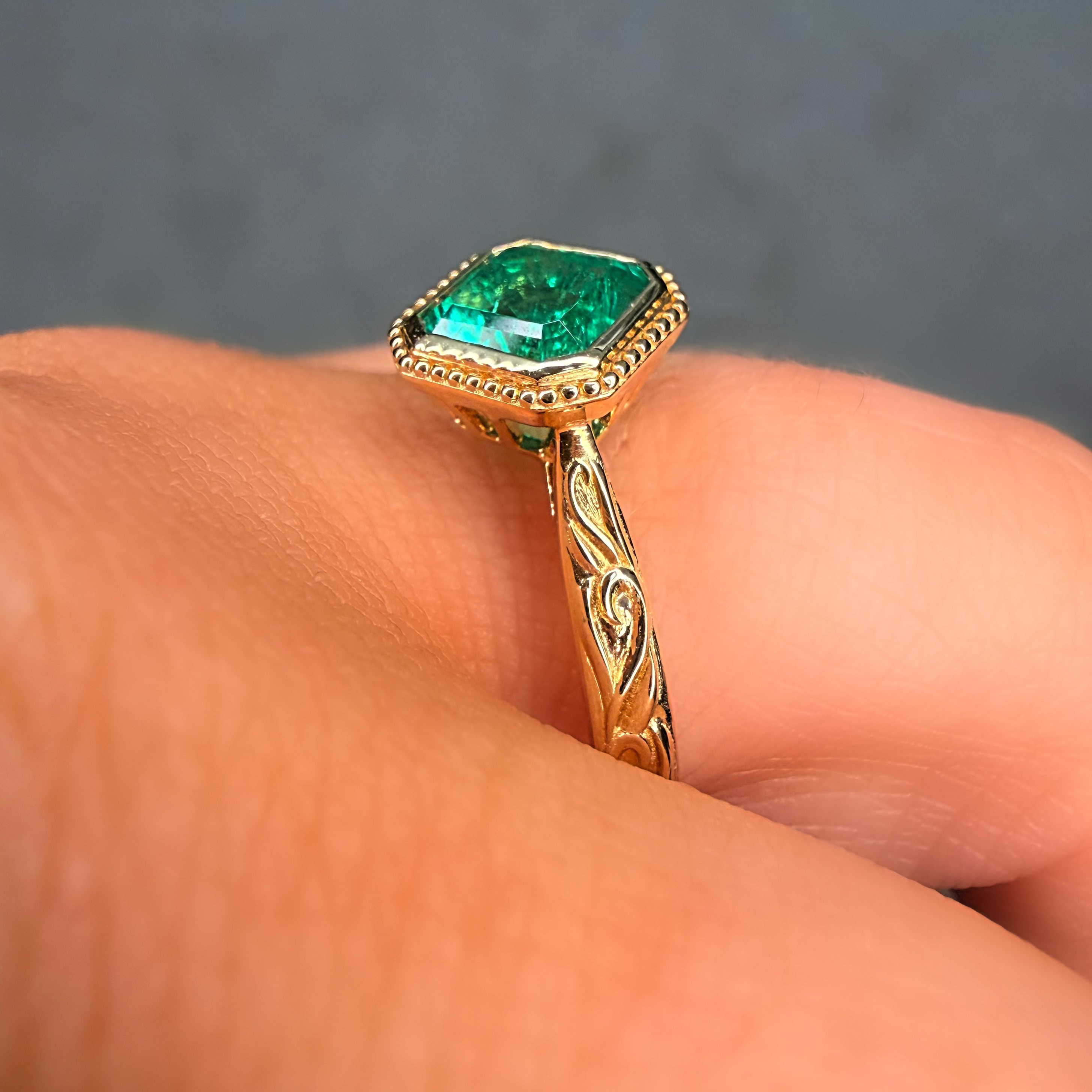 Gold ring with a green gemstone on a finger against a gray background