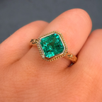 Gold ring with a green gemstone held on a hand against a dark background