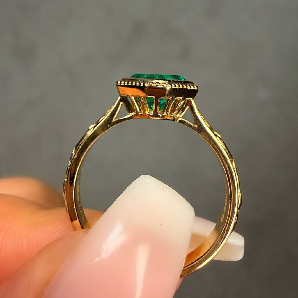 Gold ring with a green gemstone held by a hand against a gray background