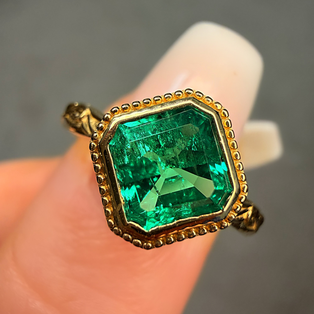 Gold ring with a green gemstone held between fingers against a neutral background