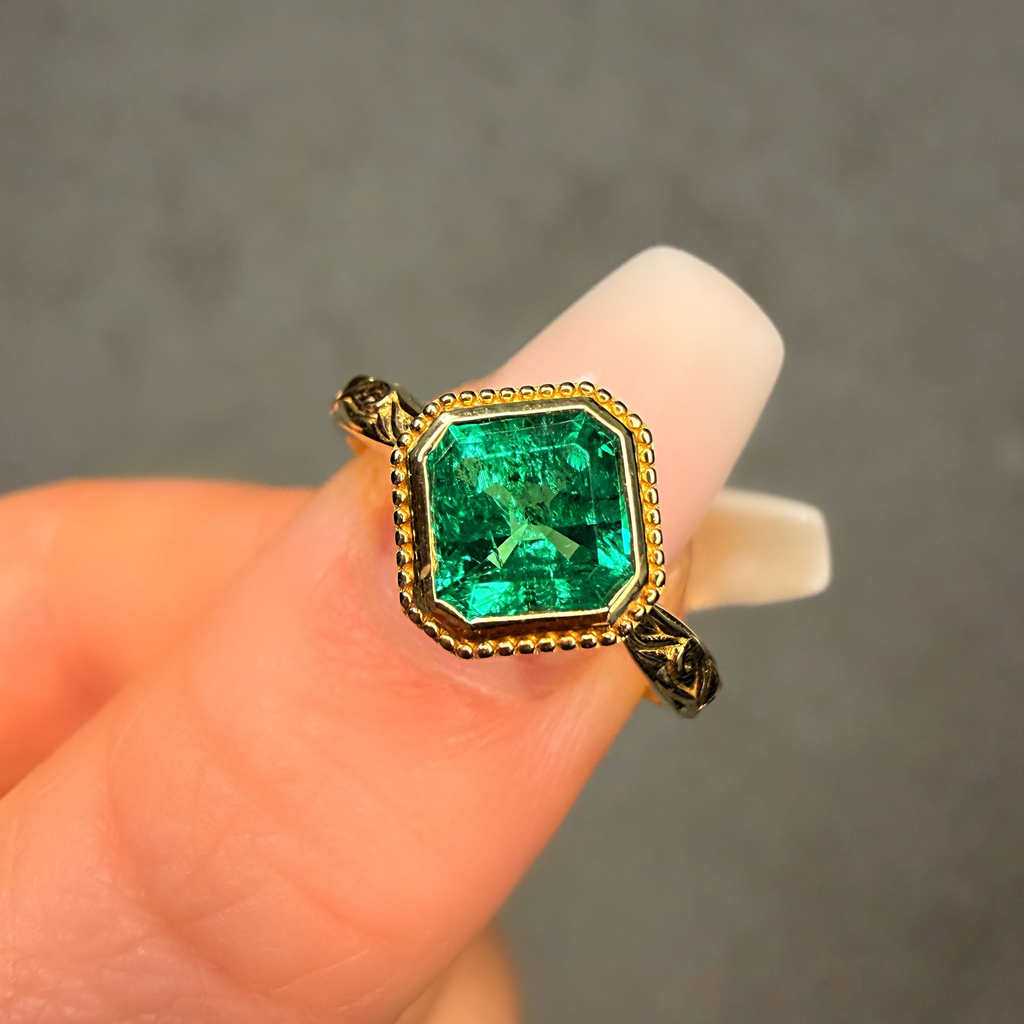 Gold ring with a green gemstone held between fingers against a neutral background