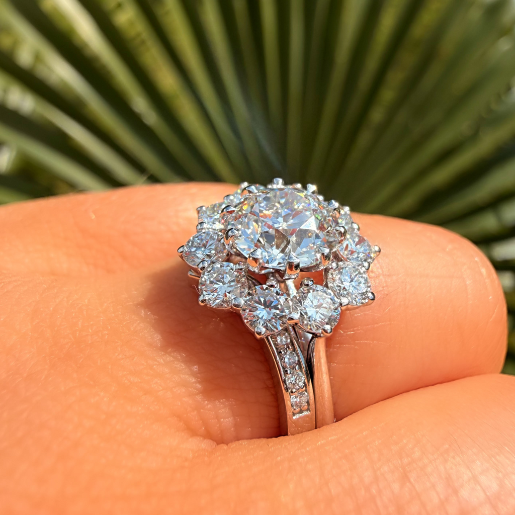Diamond ring held on a person's finger with a blurred green leaf background