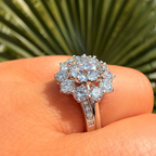 Diamond ring held on a person's finger with a blurred green leaf background