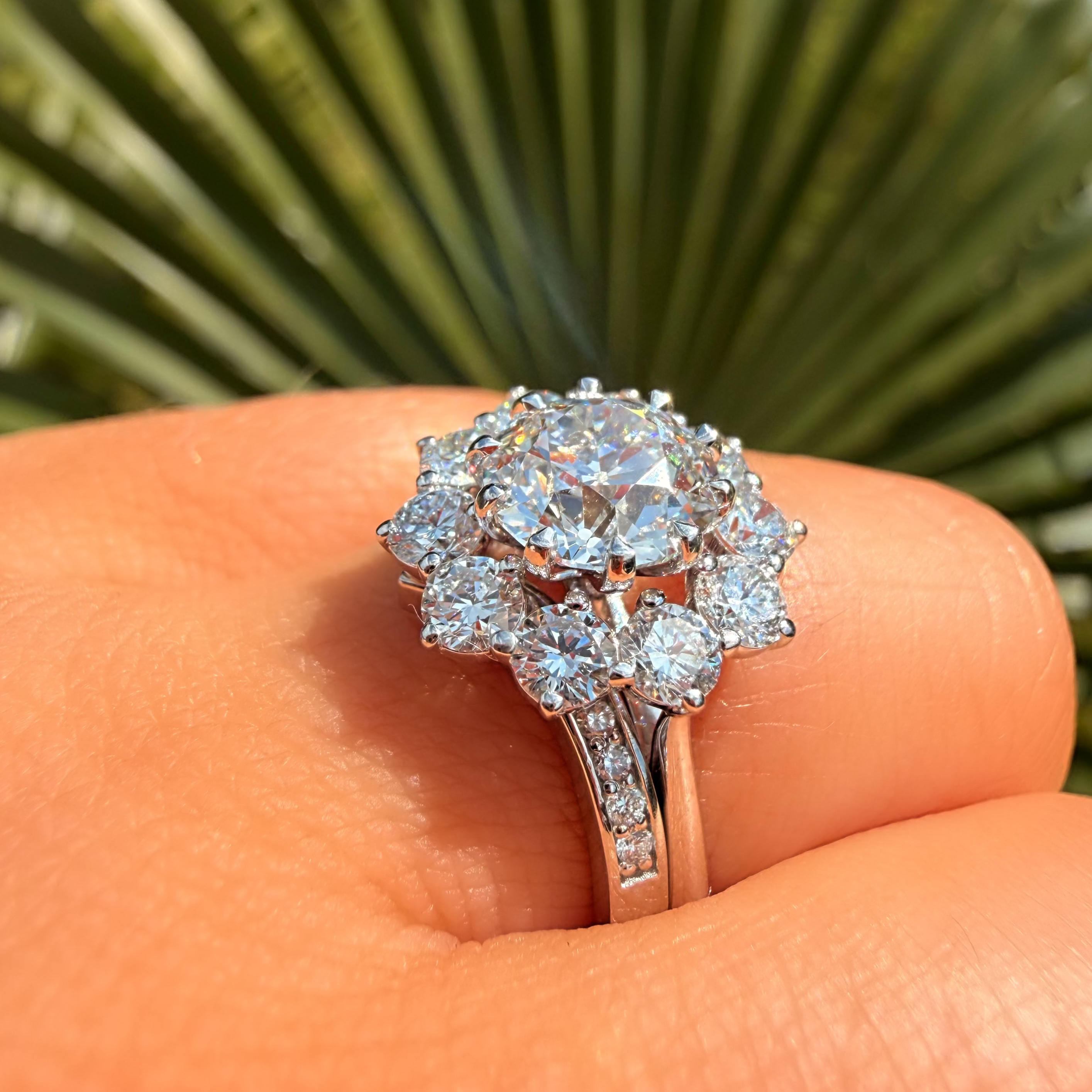 Diamond ring held on a person's finger with a blurred green leaf background