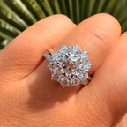 Silver ring with a large diamond on a person's finger against a green plant background