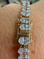 A close-up of a yellow gold tennis bracelet with marquise-cut clear gemstones worn on a person's wrist.