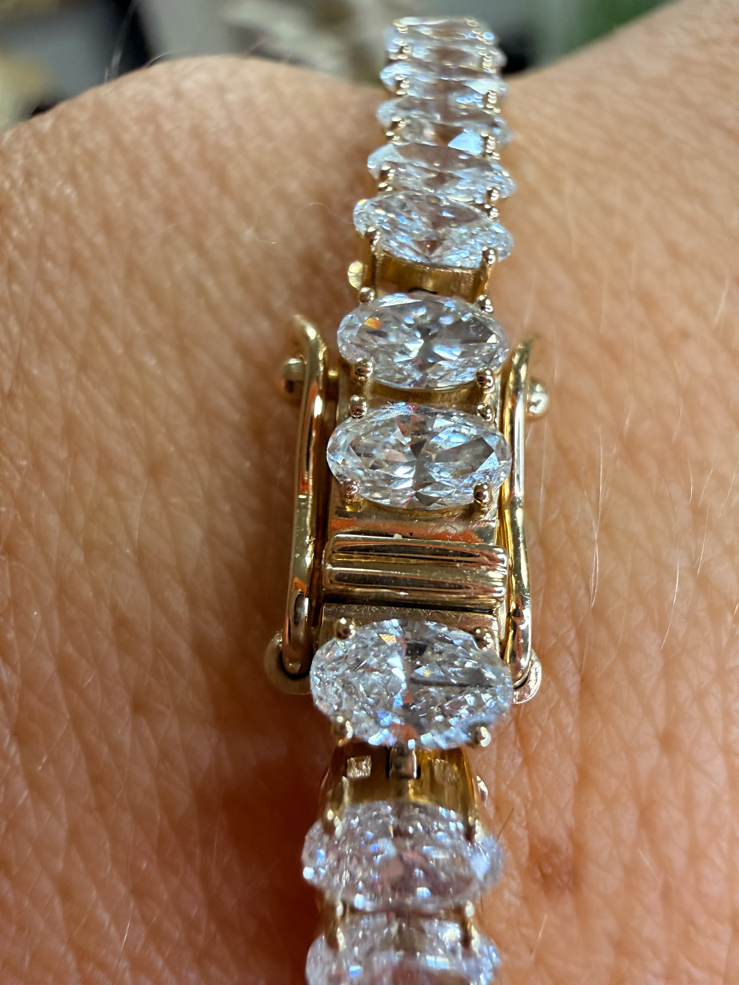 A close-up of a yellow gold tennis bracelet with marquise-cut clear gemstones worn on a person's wrist.