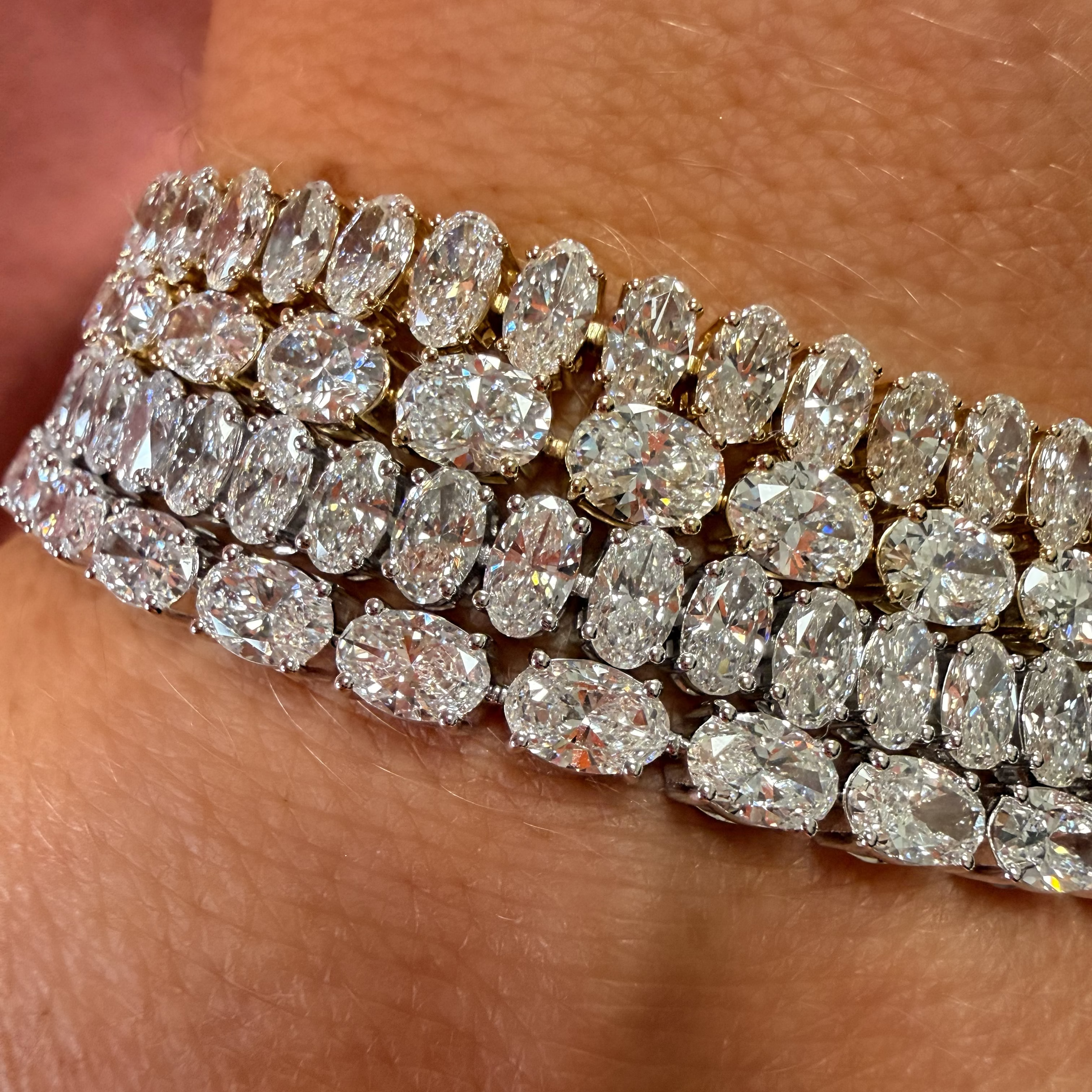 A close-up of a multi-row diamond bracelet worn on a wrist, featuring marquise-cut and oval diamonds set in yellow gold.