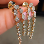 Gold earrings with teardrop-shaped diamonds held between fingers against a neutral background