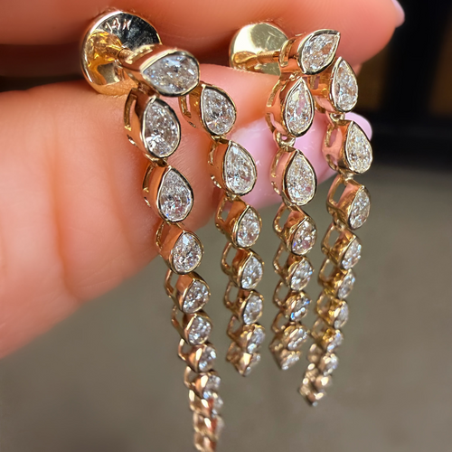 Gold earrings with teardrop-shaped diamonds held between fingers against a neutral background