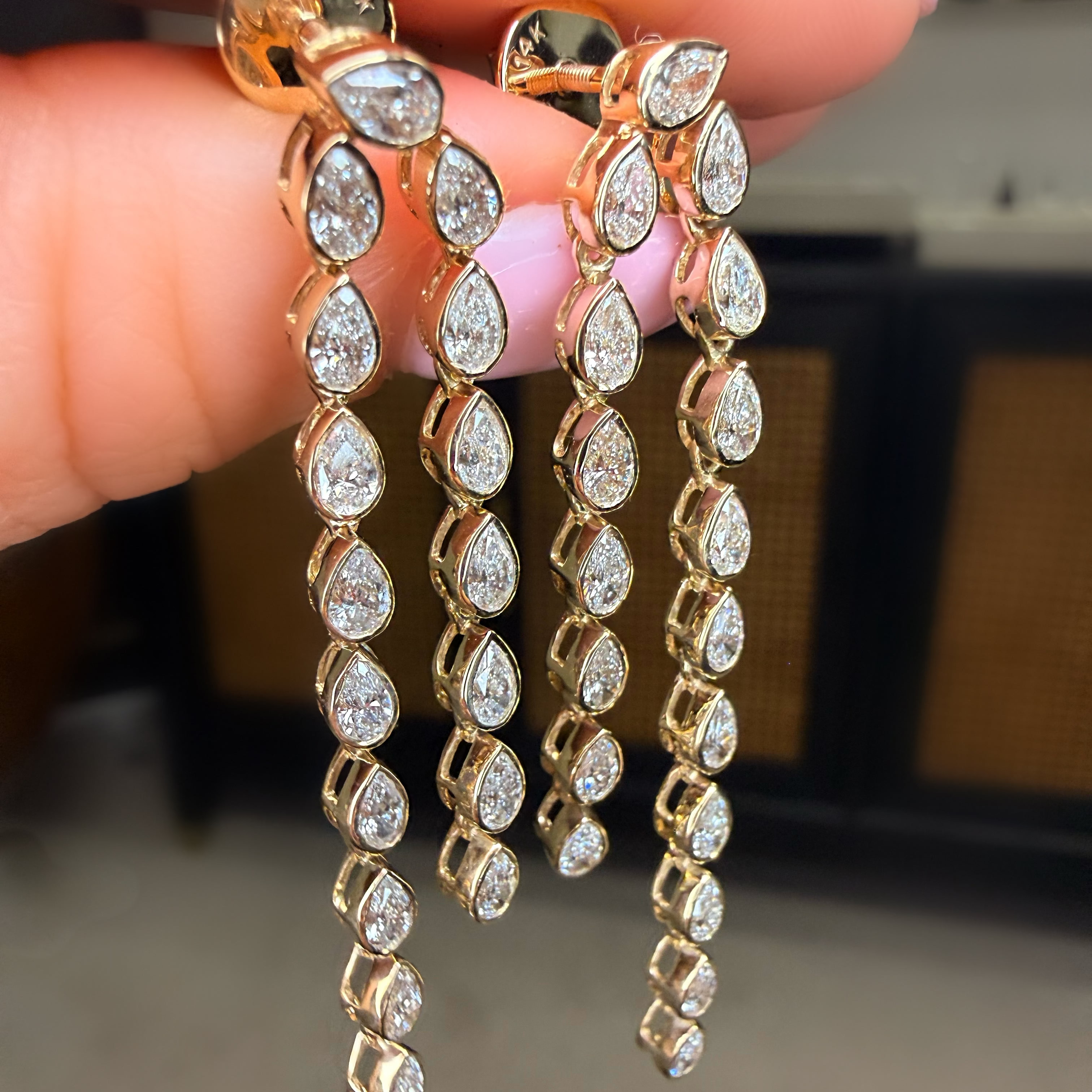 Gold earrings with clear stones held between fingers against a neutral background
