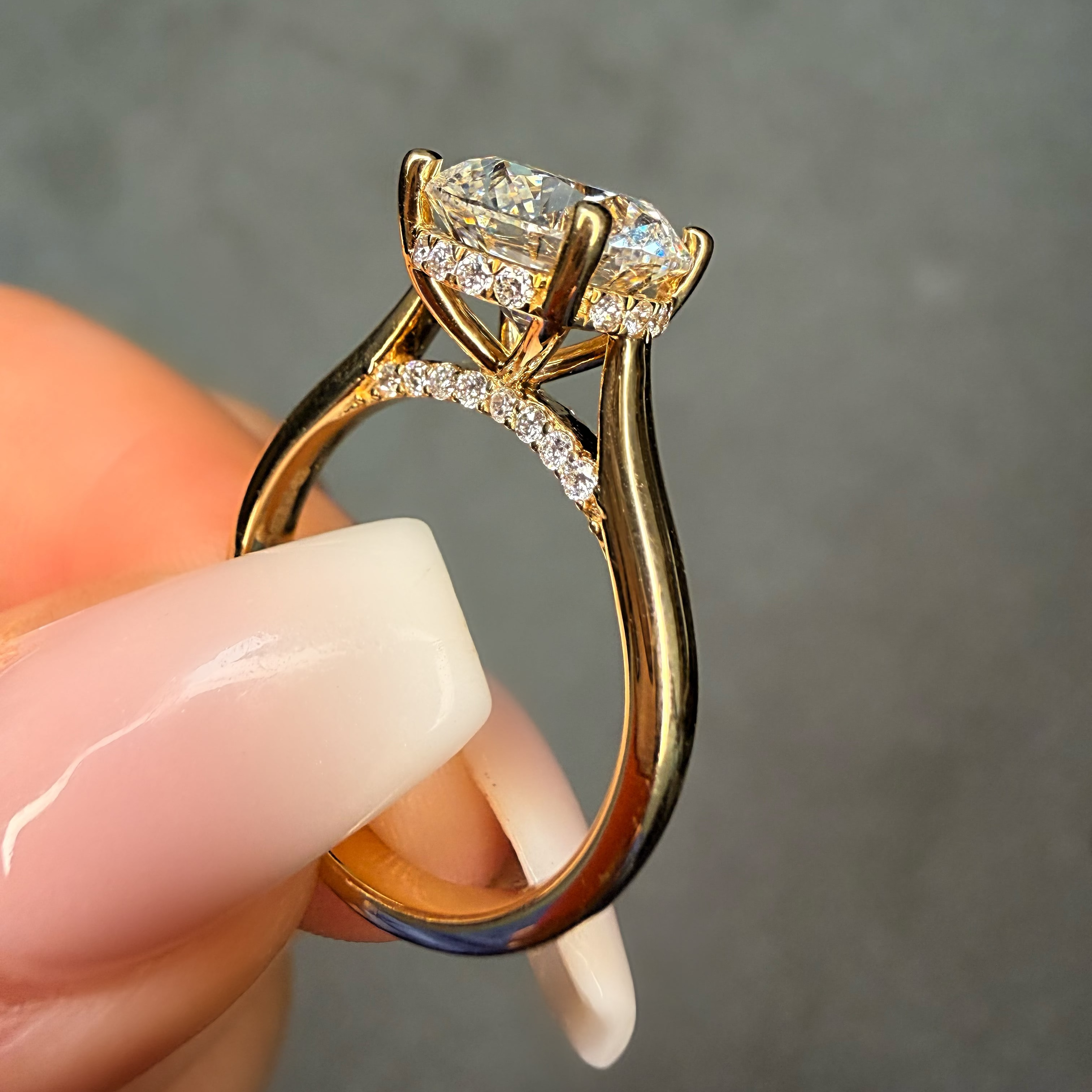 Gold ring with a large diamond held between fingers against a neutral background