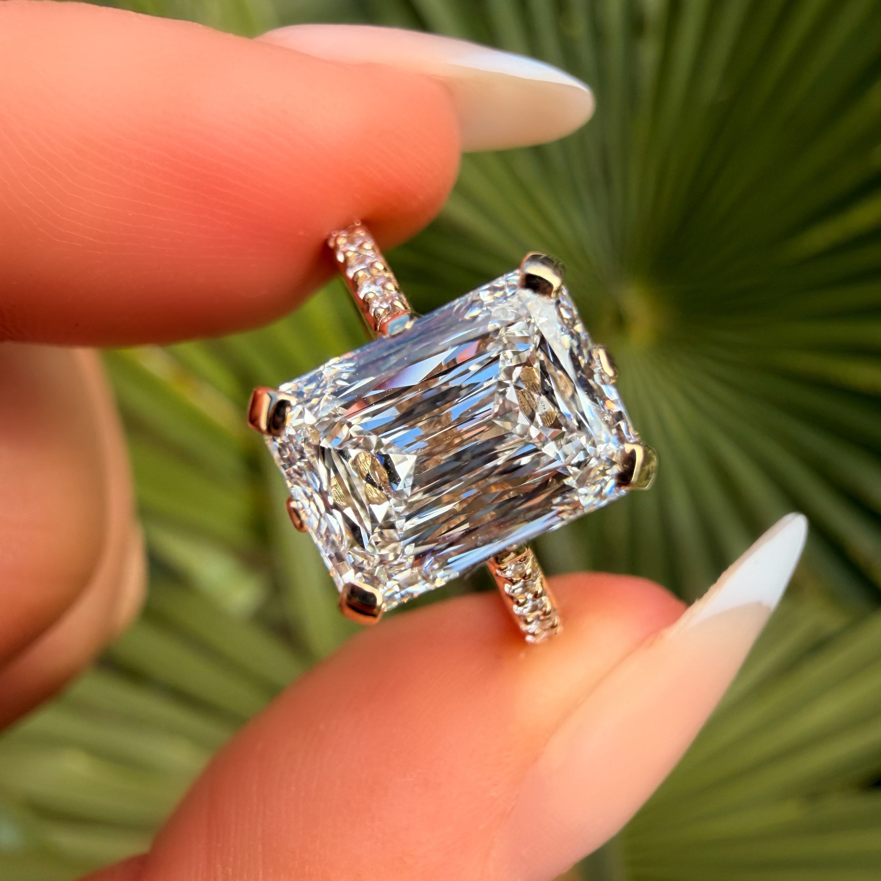 Diamond ring held between fingers with a green leafy background