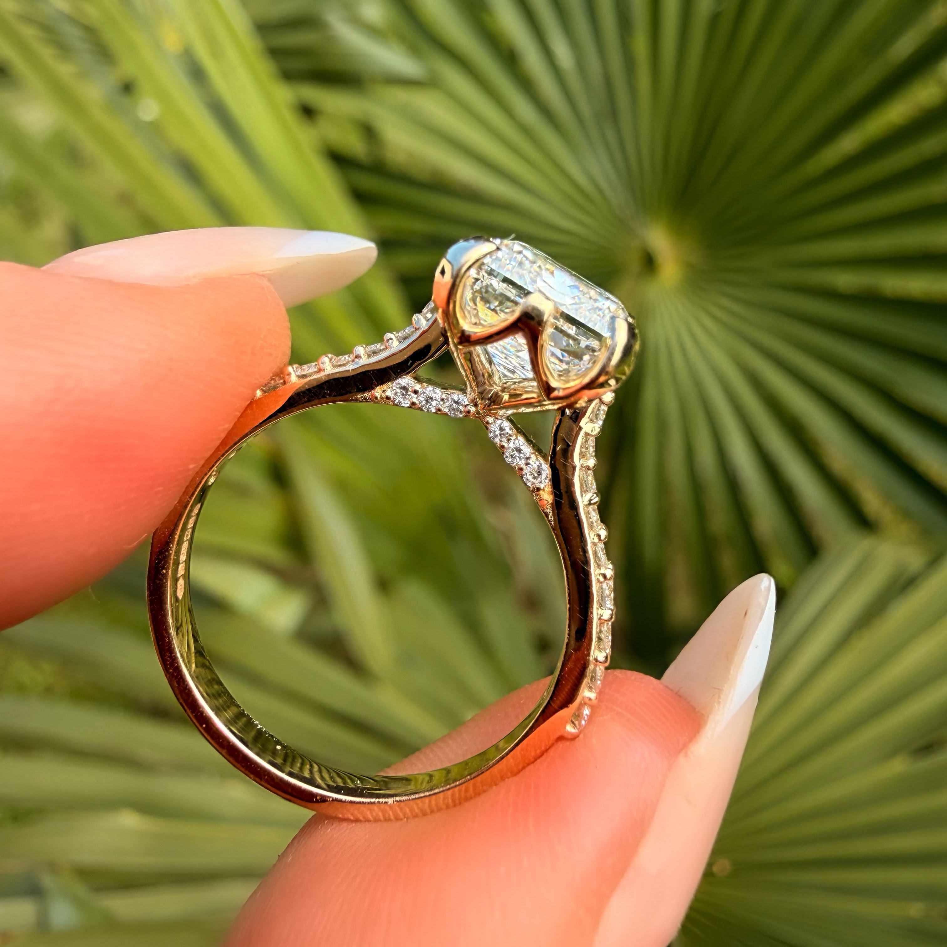 Gold ring with a diamond held by a hand against a green leafy background