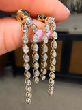 Gold earrings with clear stones held between fingers against a neutral background