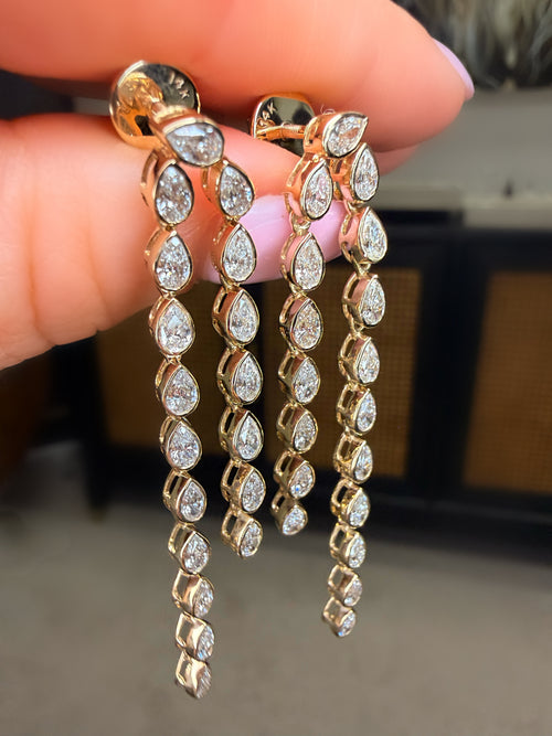 Gold earrings with clear stones held between fingers against a neutral background