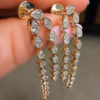 Gold earrings with teardrop-shaped diamonds held between fingers against a neutral background