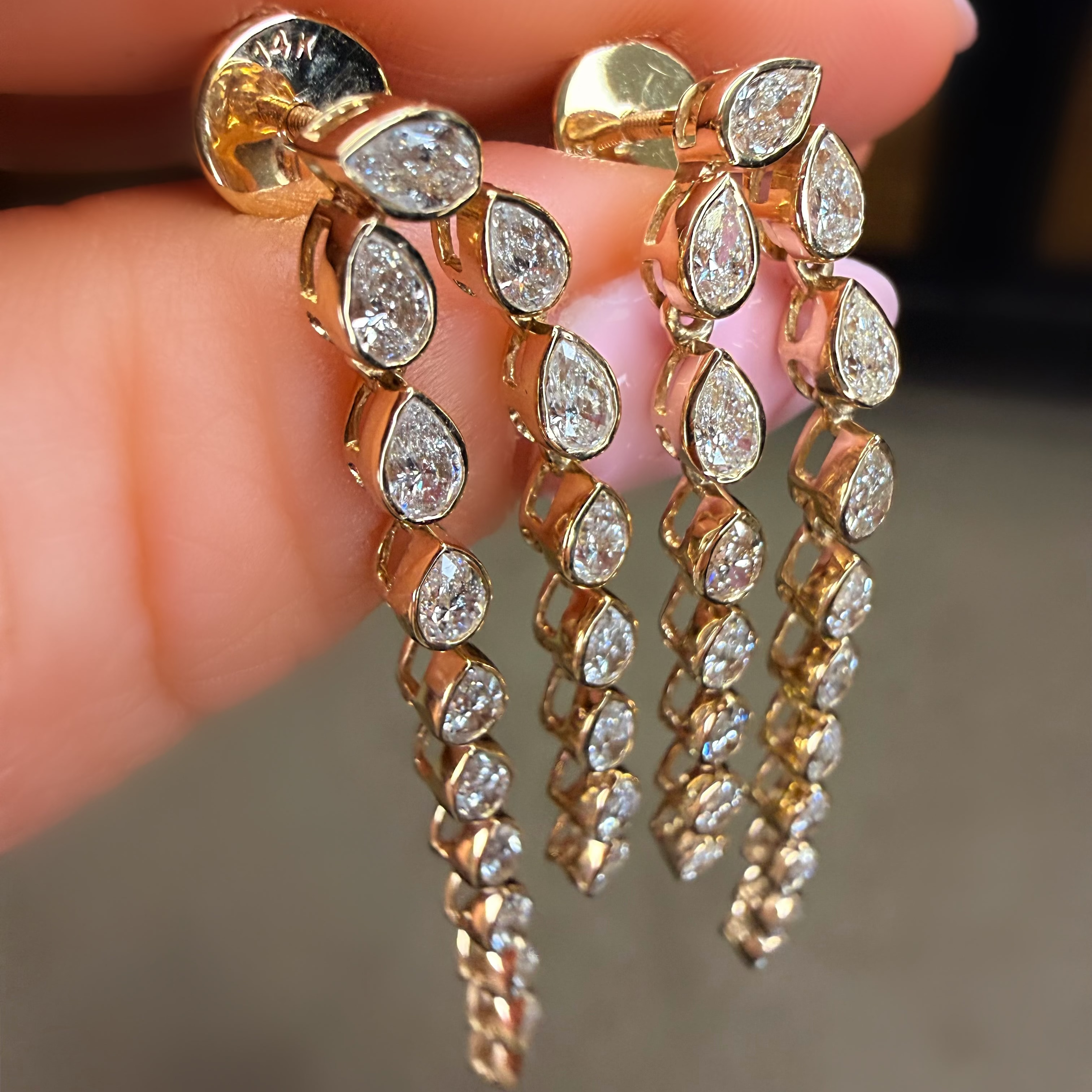Gold earrings with teardrop-shaped diamonds held between fingers against a neutral background