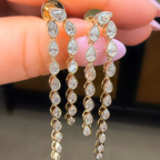 Gold and diamond earrings held between fingers against a neutral background