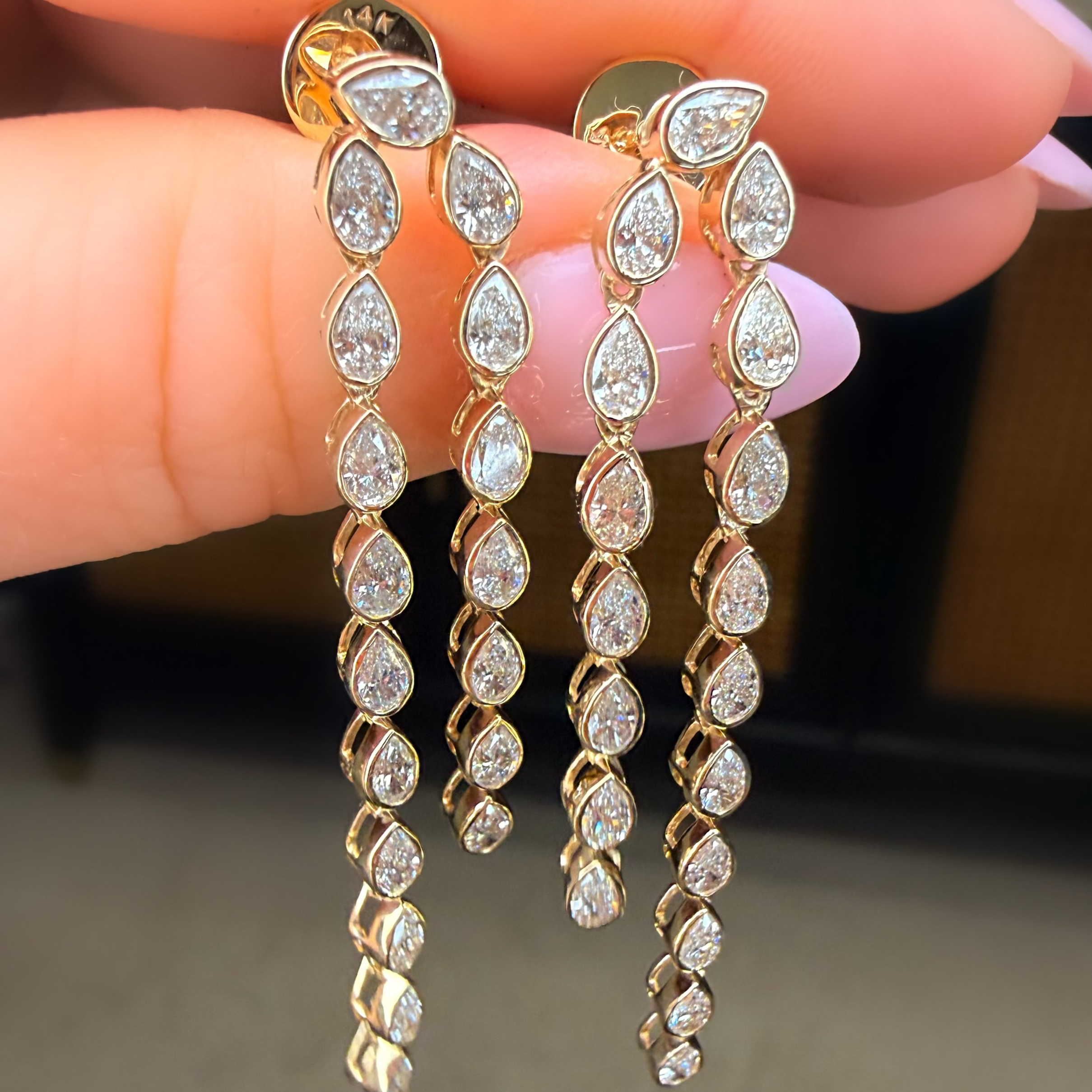 Gold and diamond earrings held between fingers against a neutral background