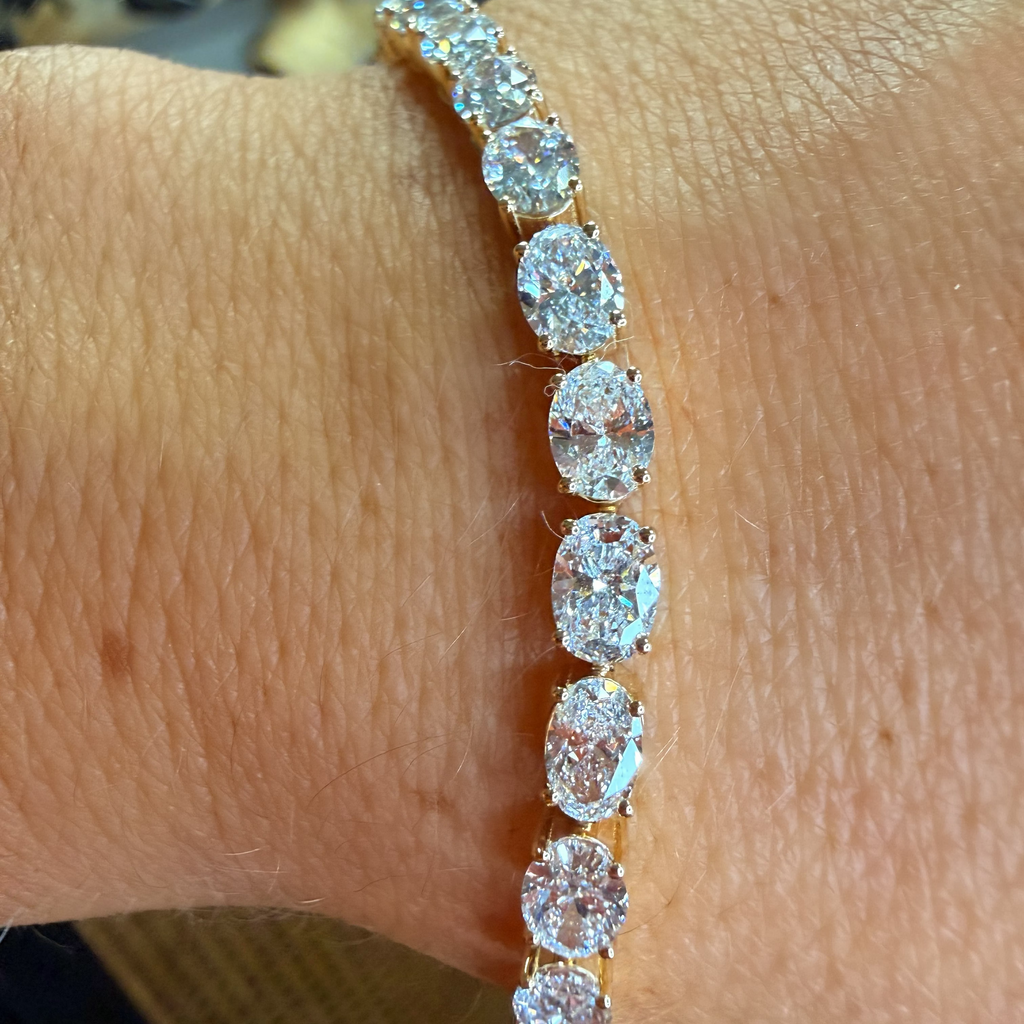 A close-up of a yellow gold tennis bracelet with seven oval-cut clear gemstones worn on a person's wrist.