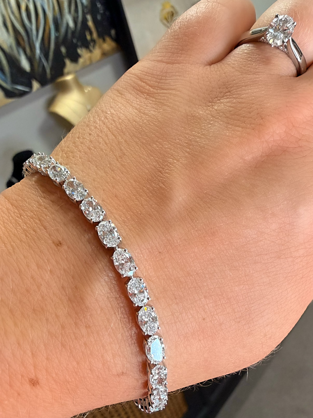A close-up of a person's wrist wearing a silver tennis bracelet with round-cut clear stones, with a matching silver ring visible on the index finger.