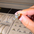 Person holding a diamond ring in front of an open jewelry box with more rings.
