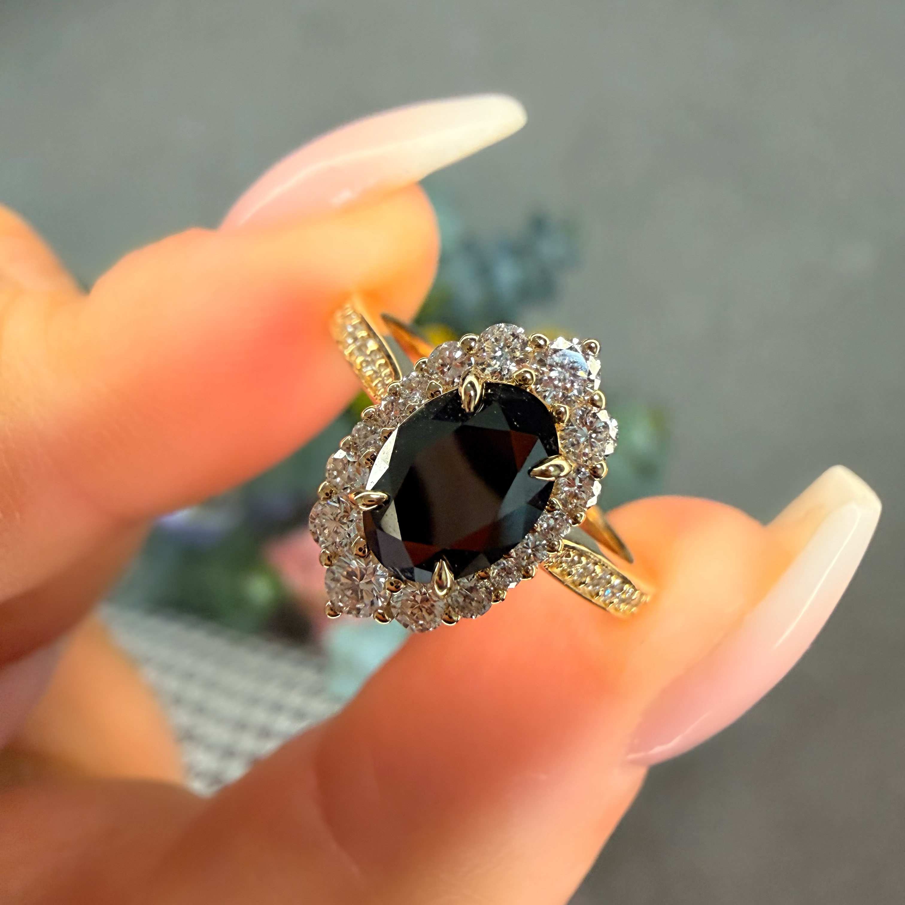 Gold ring with a black gemstone held by a hand against a blurred background