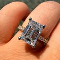 An emerald-cut diamond ring with a yellow gold band, worn on a person's finger.