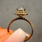 Gold ring with a diamond held between fingers against a neutral background
