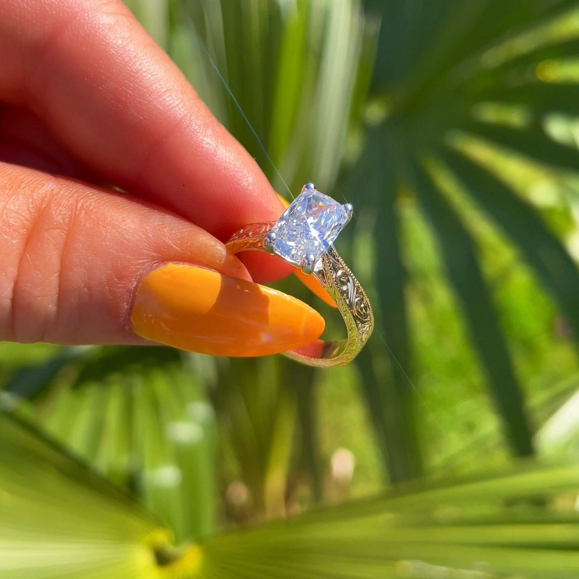 Hand holding a diamond ring with a palm leaf background