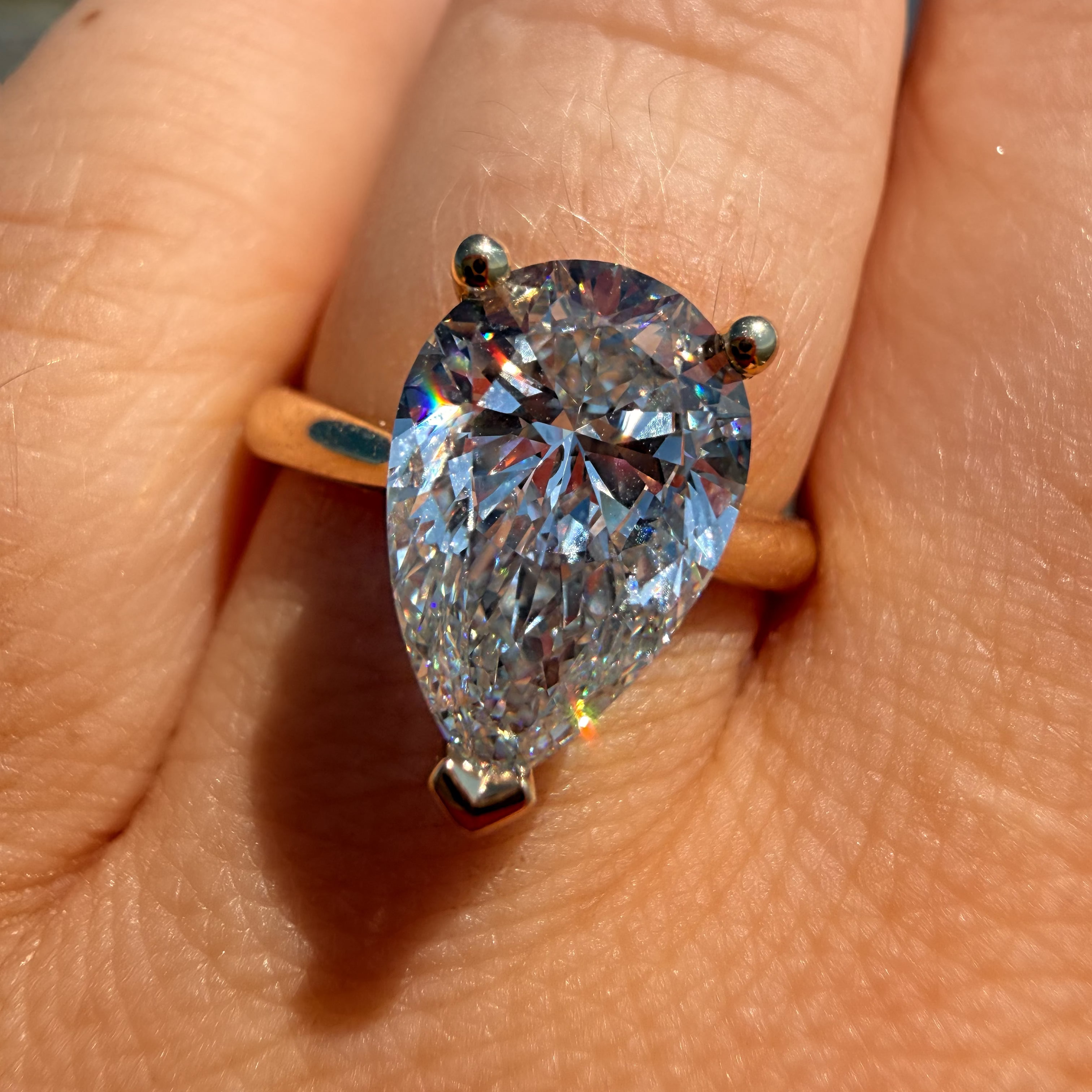 A pear-cut diamond ring with a yellow gold band, worn on a person's finger outdoors under bright sunlight.