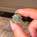 Close-up of a hand holding a ring with a green gemstone, with a jewelry box in the background.