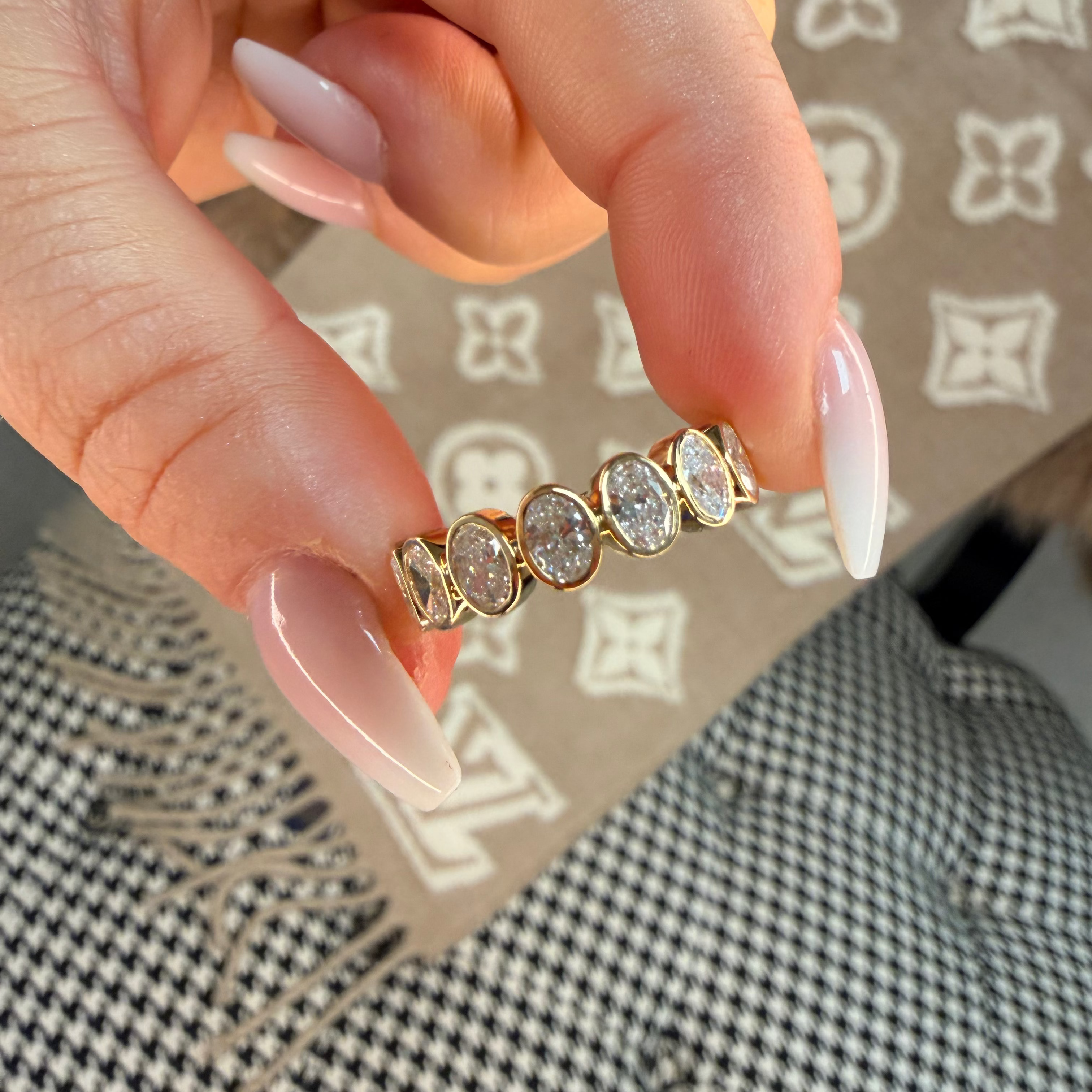 Gold ring with diamonds held by a hand against a patterned background