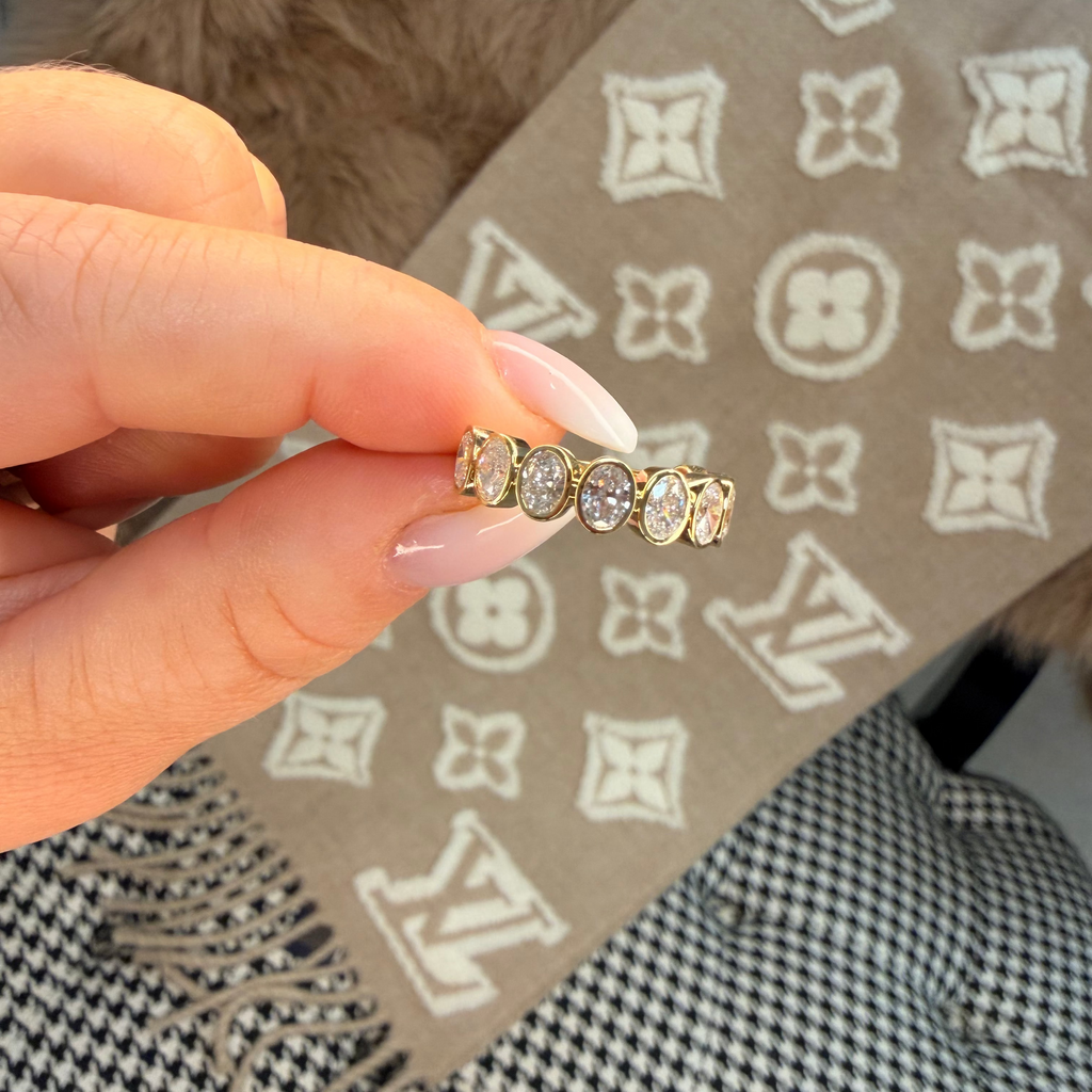 Gold ring with diamonds held by a hand on a patterned surface