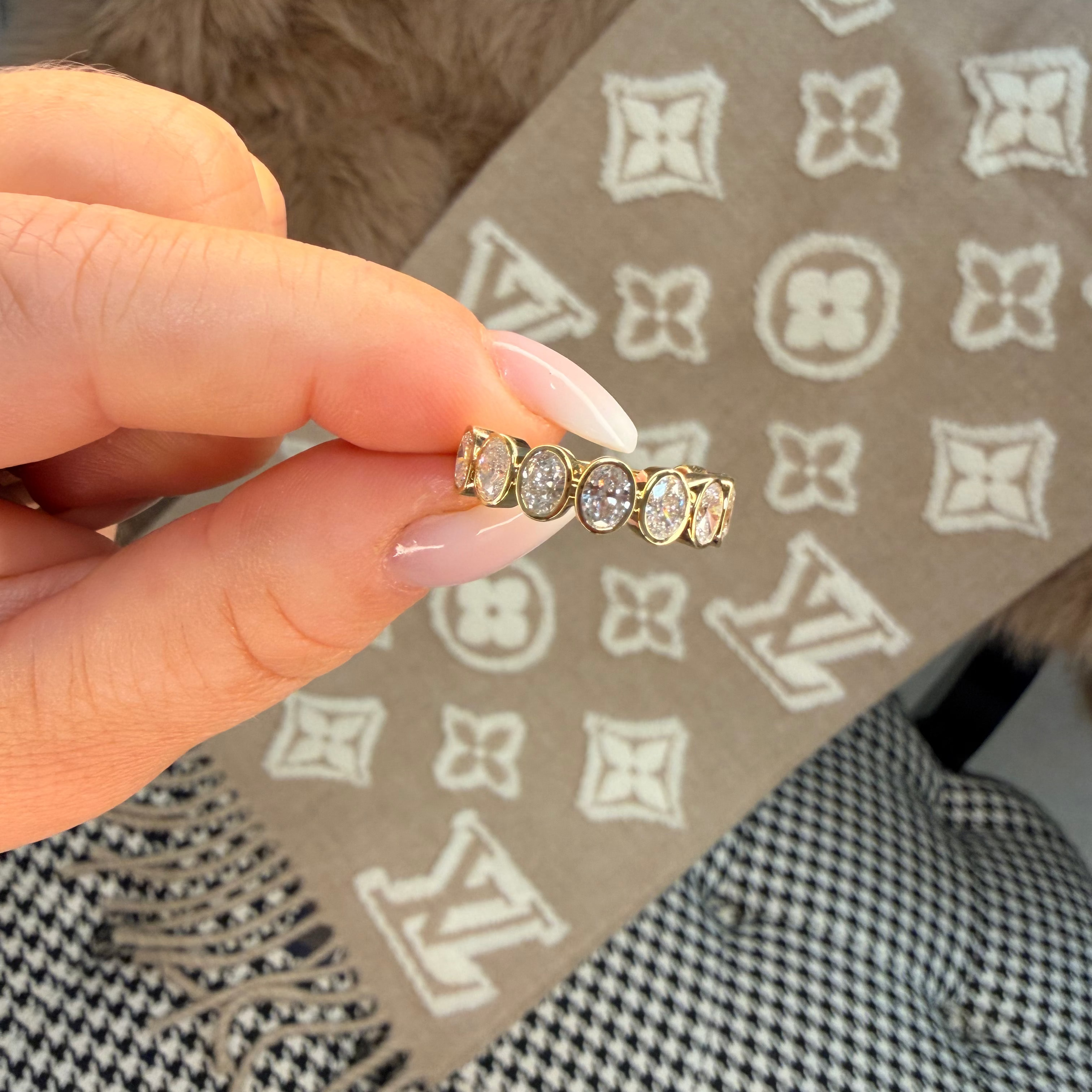 Gold ring with diamonds held by a hand on a patterned surface