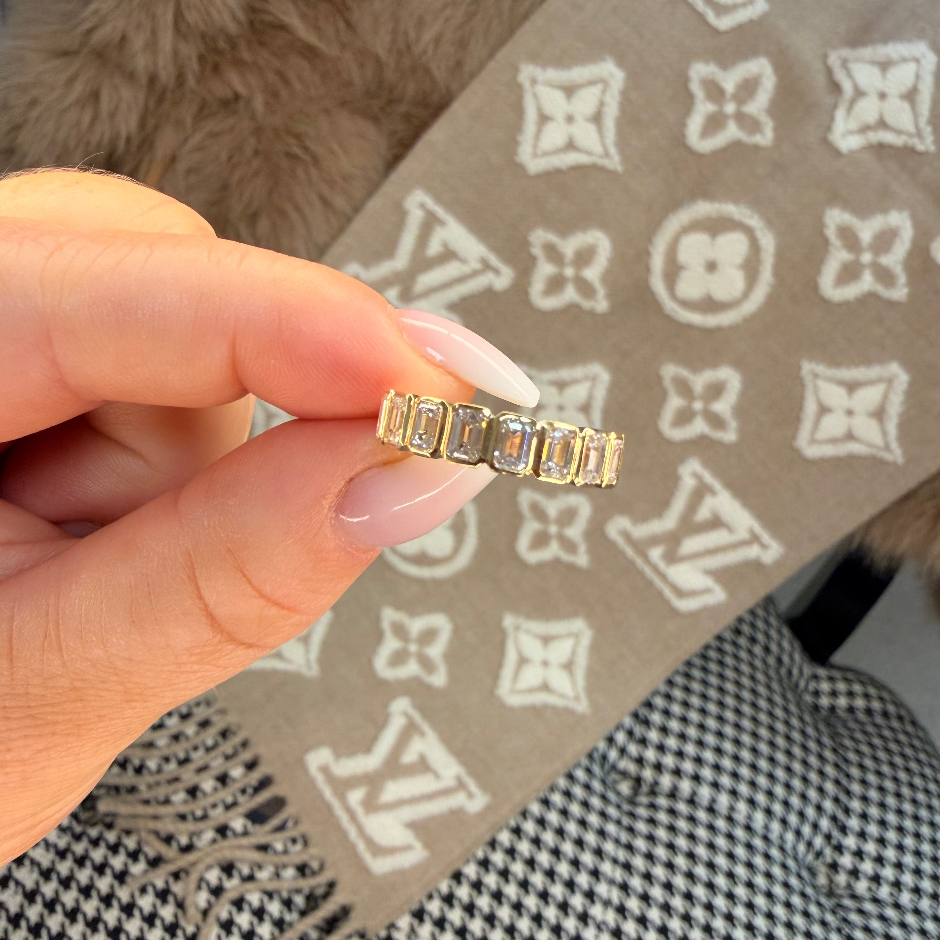 Gold ring held by a hand with a patterned fabric background