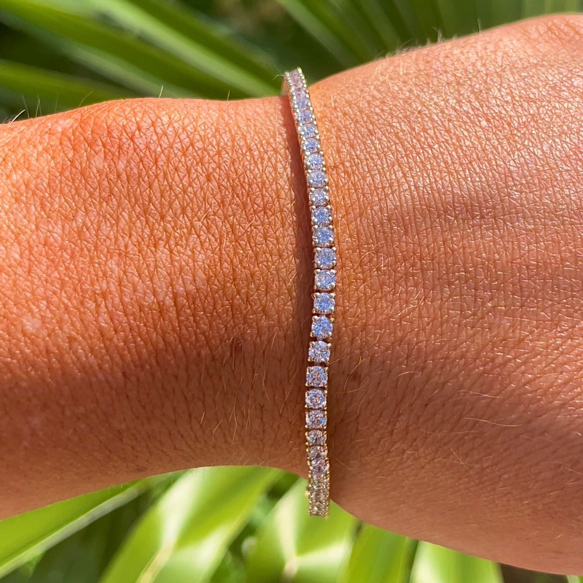 Gold bracelet on a wrist with a green leafy background