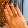 Hand wearing a yellow gemstone ring with red nail polish against a textured wall.