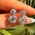 Gold and diamond stud earrings held between fingers with a natural background