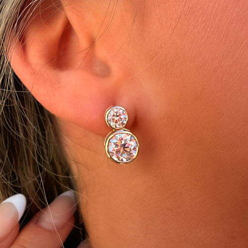 Close-up of a person wearing gold earrings with clear gemstones.