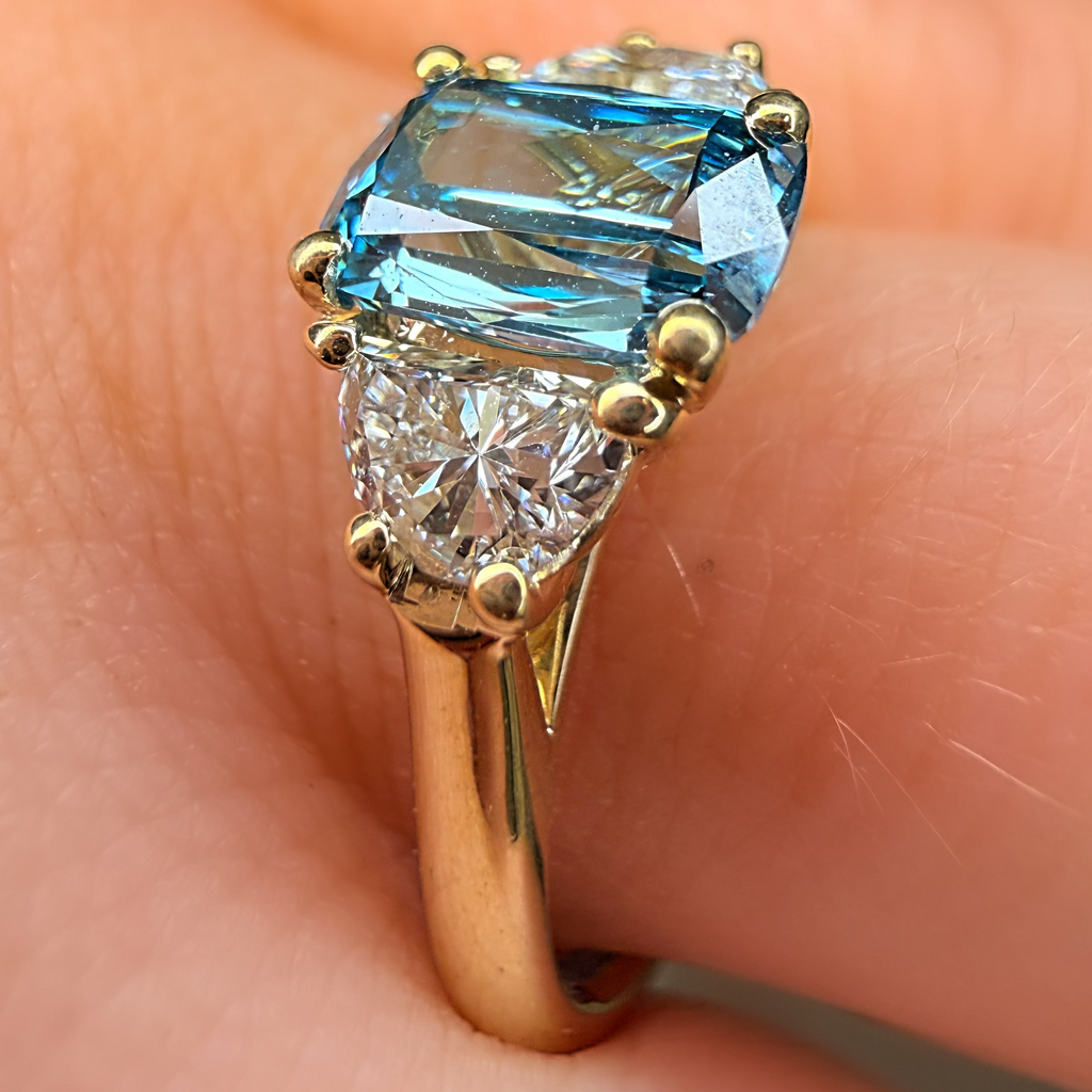 Gold ring with a blue gemstone and smaller diamond on a finger