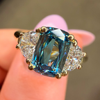 Ring with a blue gemstone and diamonds held on a finger against a blurred background