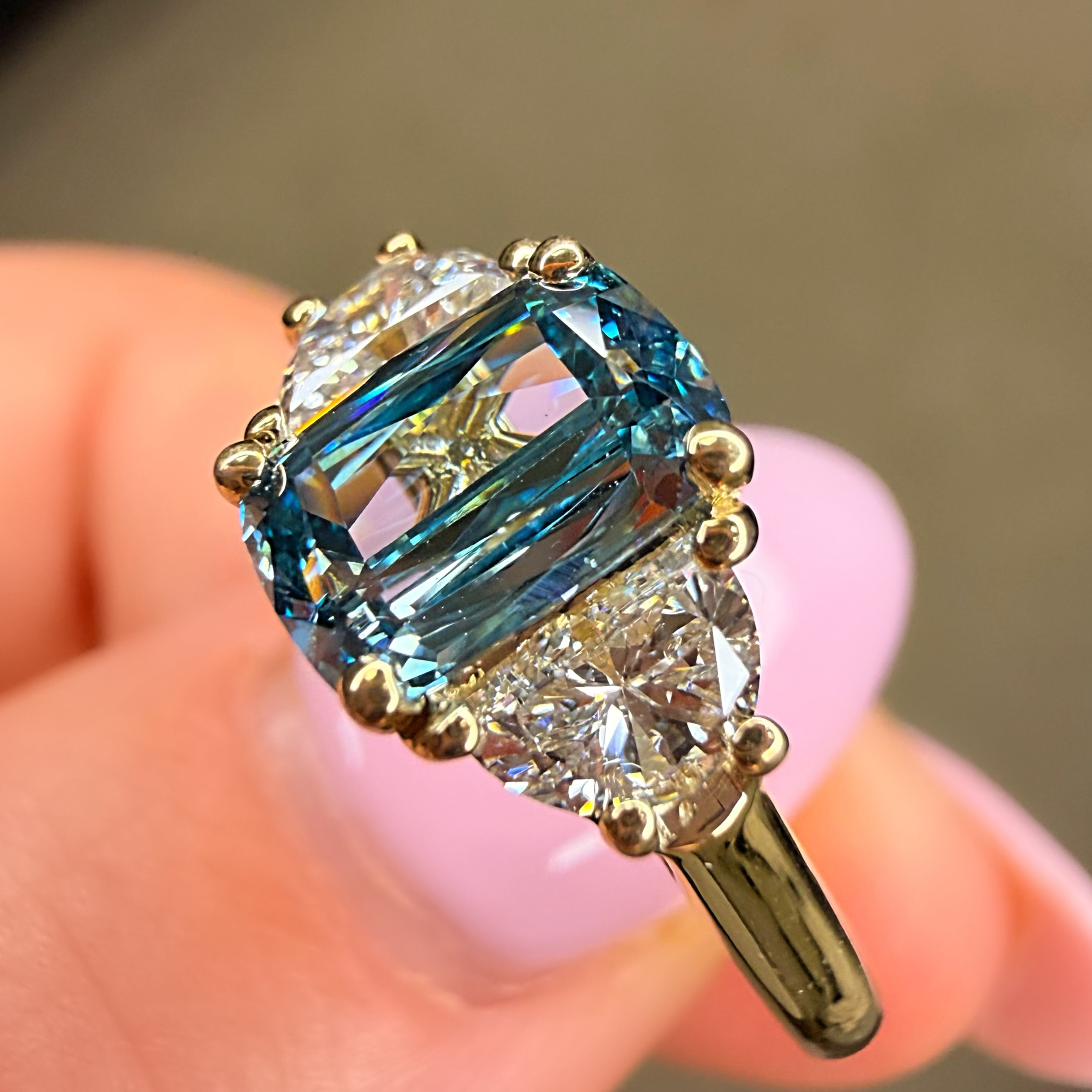 Gold ring with a large blue gemstone held in a hand against a blurred background