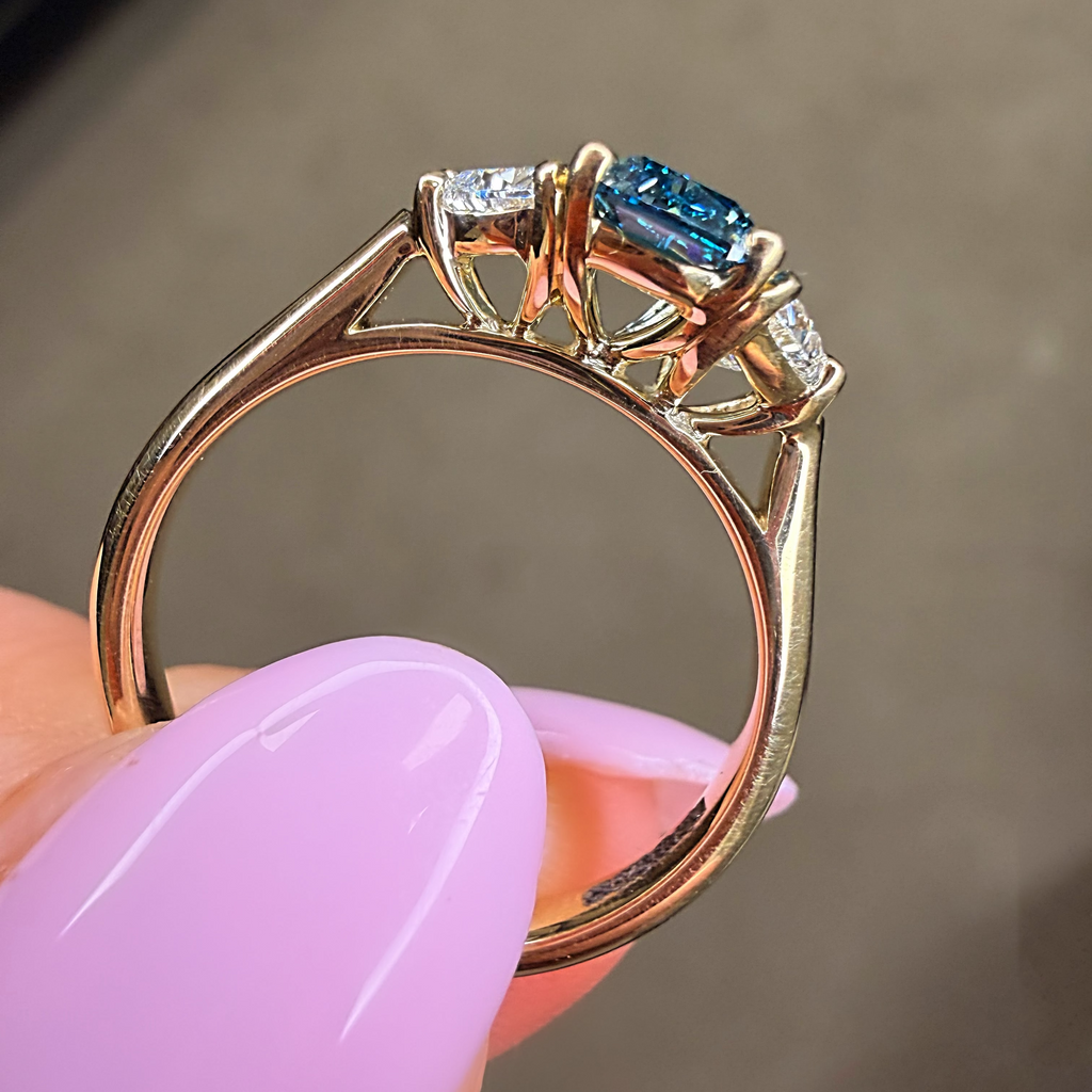 Gold ring with blue gemstone held by a hand against a blurred background