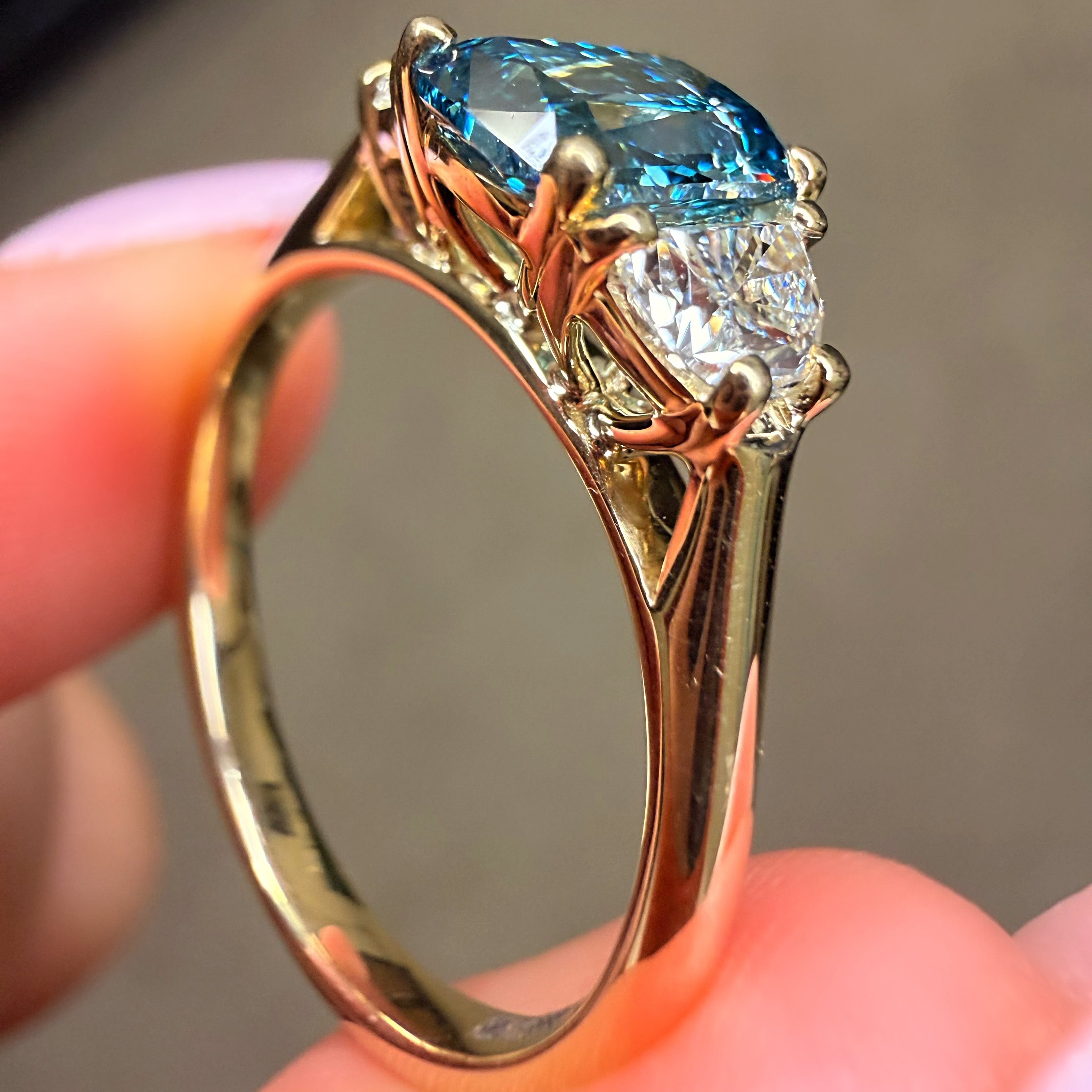 Gold ring with a blue gemstone held between fingers against a blurred background