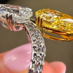 Close-up of a diamond ring with a yellow gemstone held by a hand.