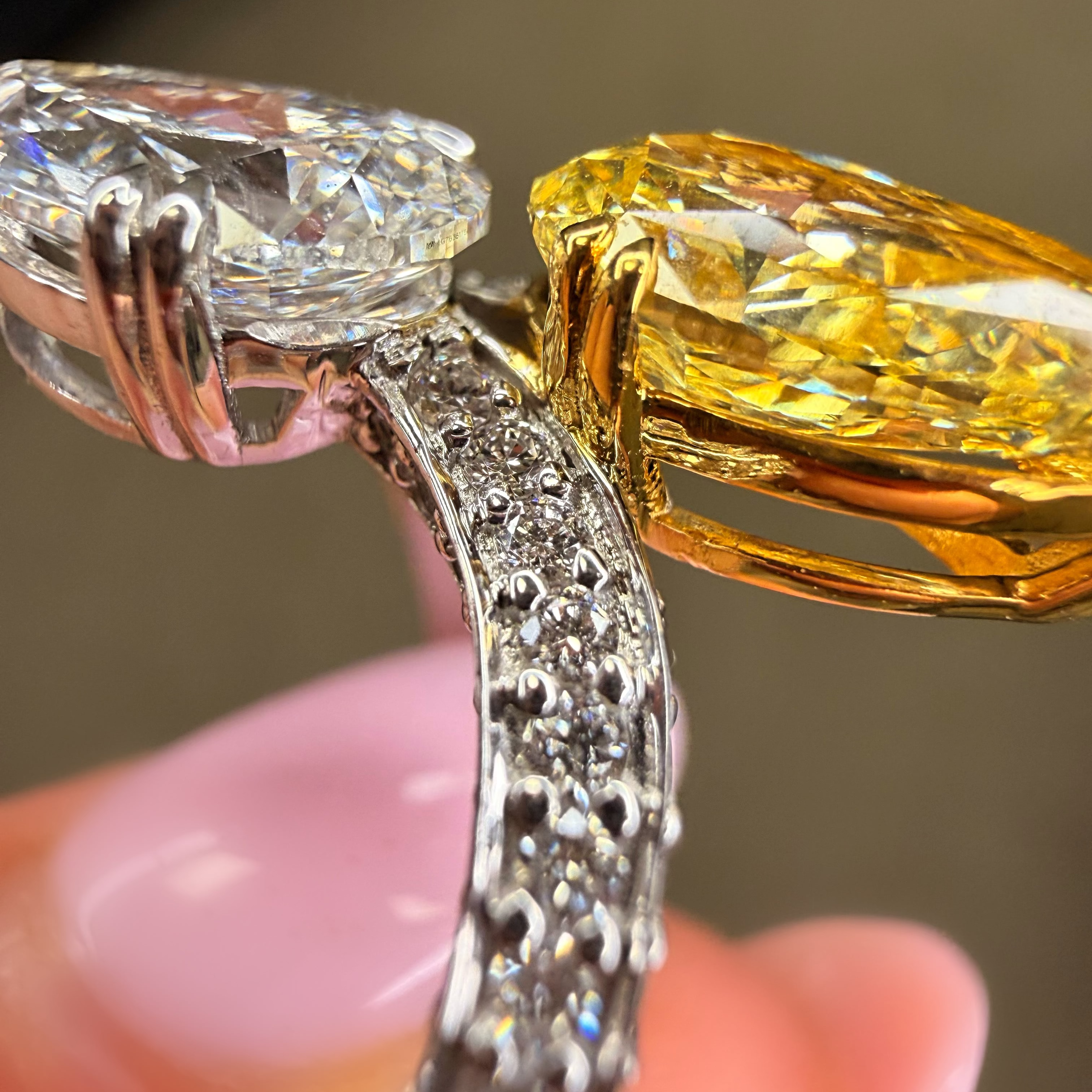 Close-up of a diamond ring with a yellow gemstone held by a hand.